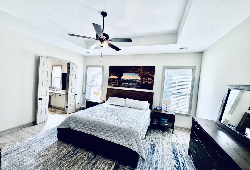 Bedroom featuring light wood finished floors, a ceiling fan, a raised ceiling, and connected bathroom