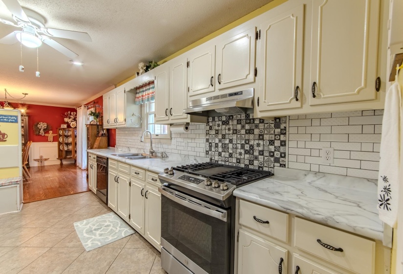 Kitchen with gas range, backsplash, light tile patterned floors, under cabinet range hood, and a ceiling fan