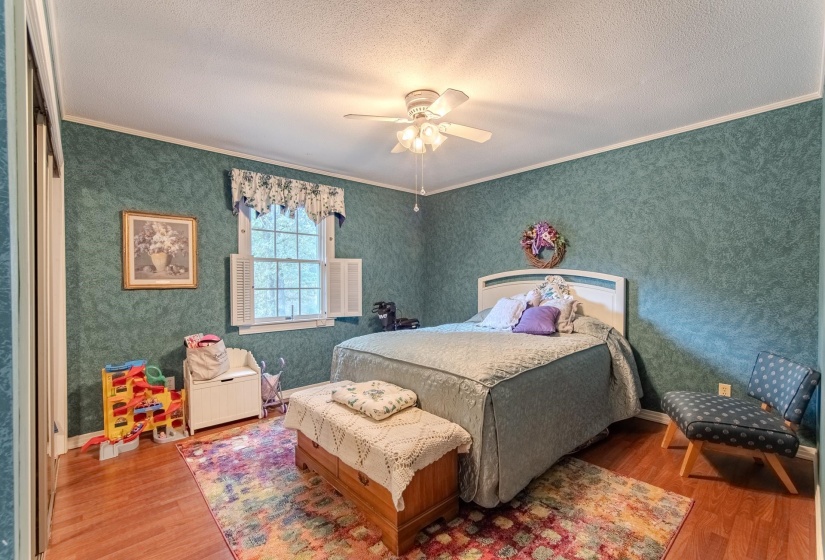 Bedroom featuring crown molding, wood finished floors, ceiling fan, a textured ceiling, and wallpapered walls