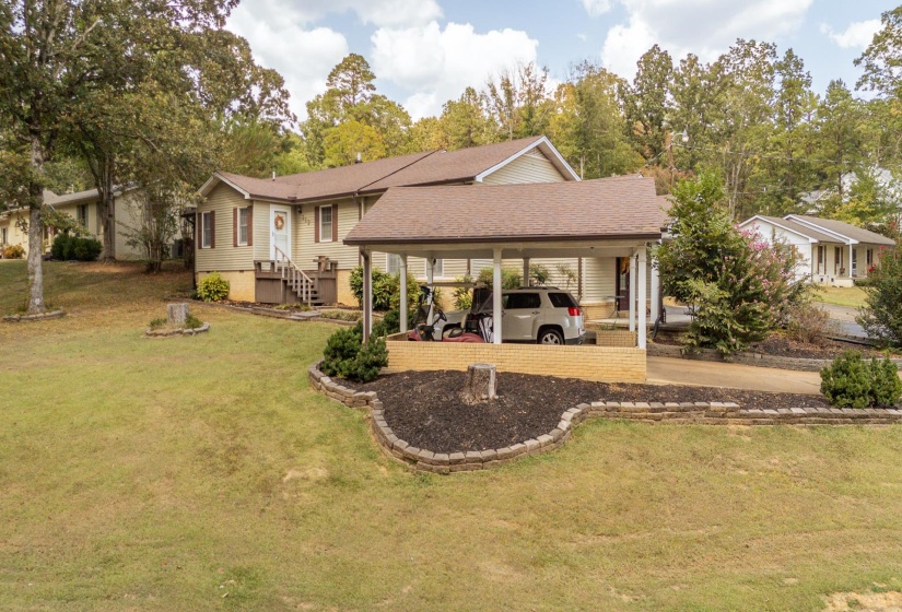house featuring a carport, concrete driveway, a lawn, roof with shingles, and view of wooded area