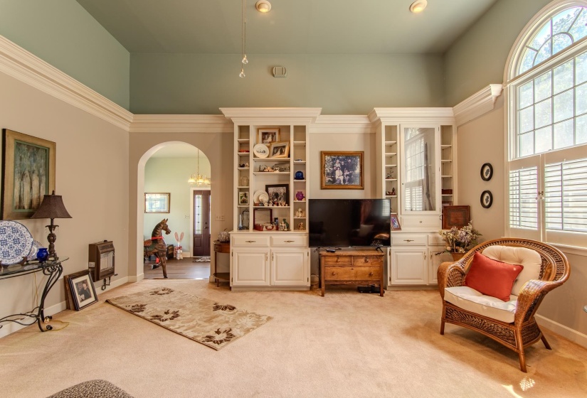 Living room with arched walkways, healthy amount of natural light, light colored carpet, recessed lighting, and a towering ceiling