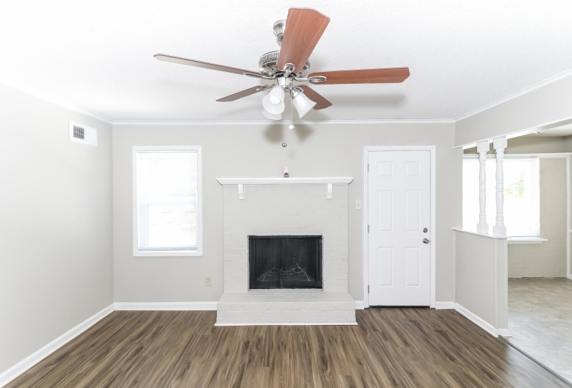 Unfurnished living room featuring dark wood-style floors, a brick fireplace, ornamental molding, and ceiling fan