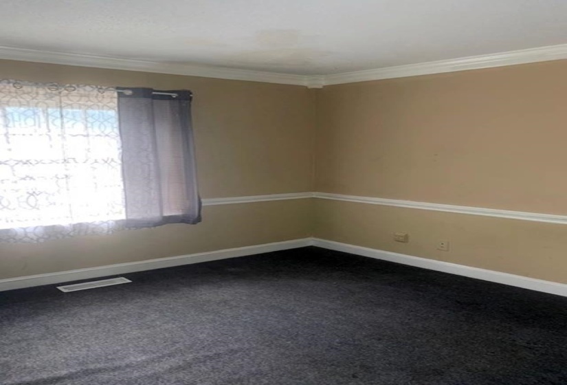 Spare room with ornamental molding and dark colored carpet