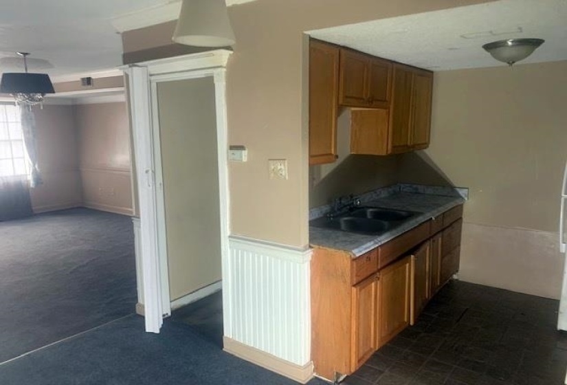 Kitchen with brown cabinets, dark colored carpet, a wainscoted wall, decorative light fixtures, and dark countertops