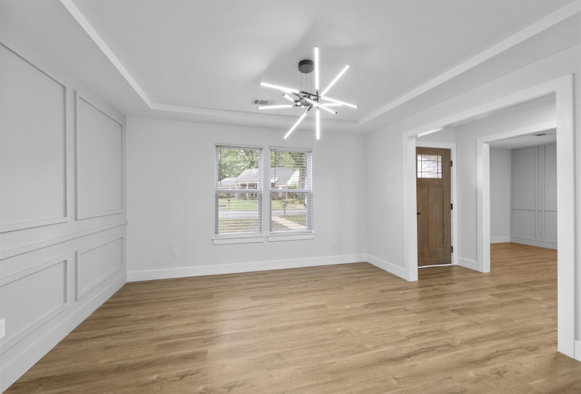 Empty room with a chandelier, a raised ceiling, and light wood-style floors