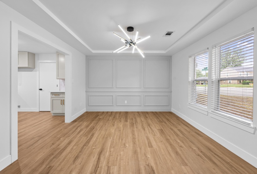 Unfurnished dining area with a chandelier, light wood-style flooring, and a raised ceiling