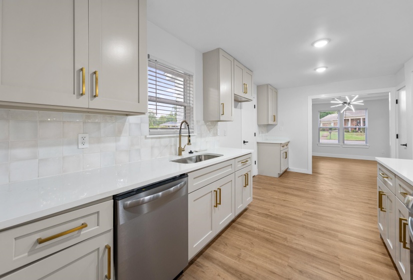 Kitchen featuring tasteful backsplash, dishwasher, light wood-type flooring, and light stone counters