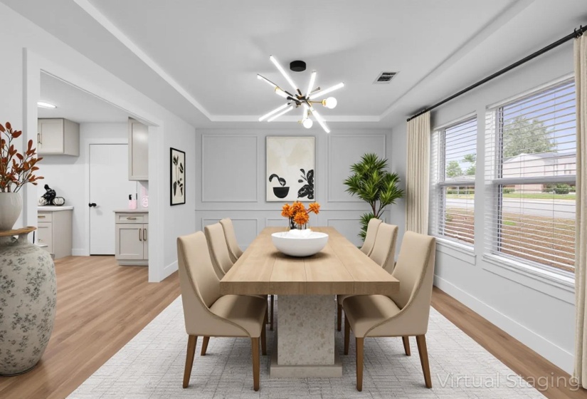 Dining room with light wood finished floors, a raised ceiling, a chandelier, and a decorative wall
