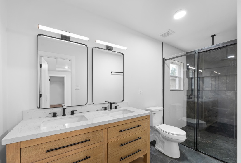 Full bath with a stall shower, double vanity, and dark tile patterned floors