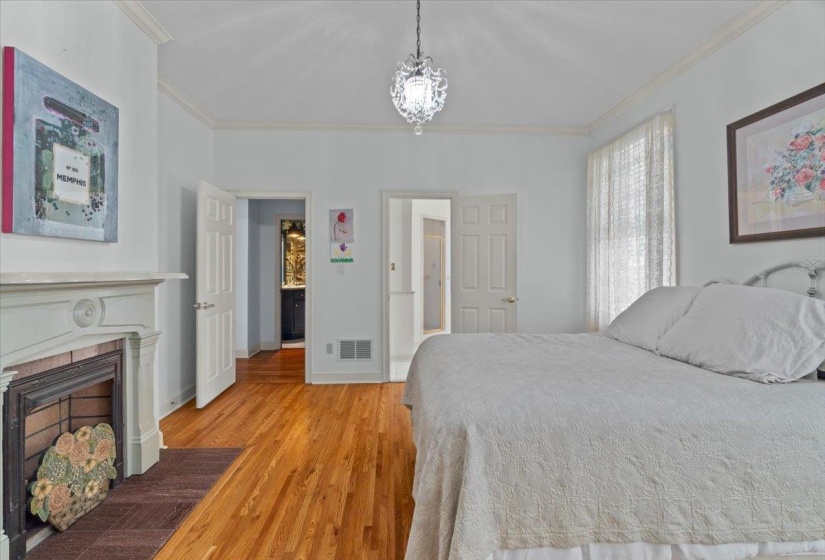 Bedroom with light wood-style flooring, crown molding, a fireplace with flush hearth, and a chandelier