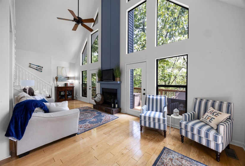 Living area featuring high vaulted ceiling, a ceiling fan, light wood-style floors, a fireplace, and stairs