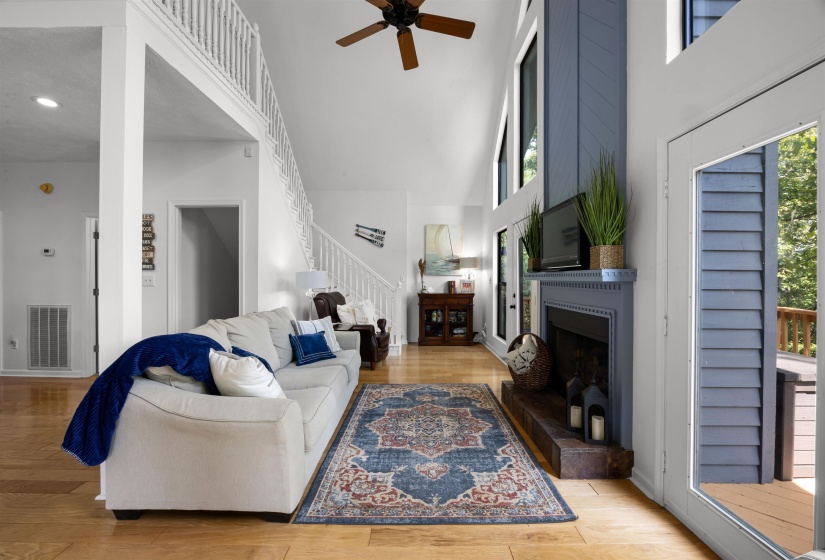 Living room featuring light wood finished floors, a large fireplace, a towering ceiling, stairway, and a ceiling fan