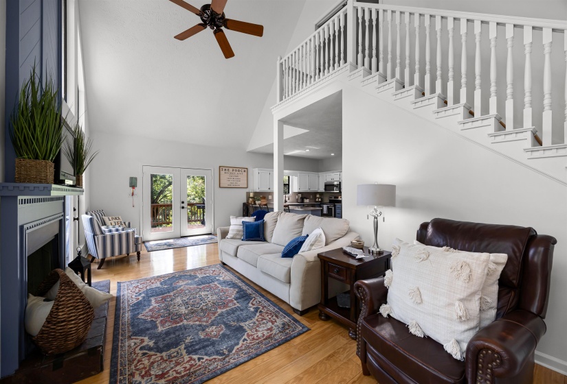Living room featuring a high ceiling, wood finished floors, french doors, a fireplace with raised hearth, and ceiling fan