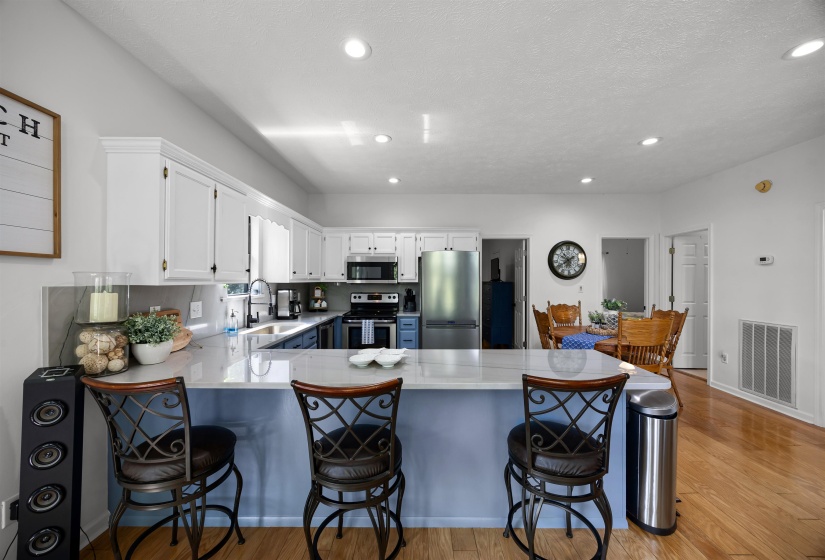 Kitchen with a peninsula, quartzite countertops, white upper and blue lower cabinetry, stainless steel appliances, and light wood-style flooring