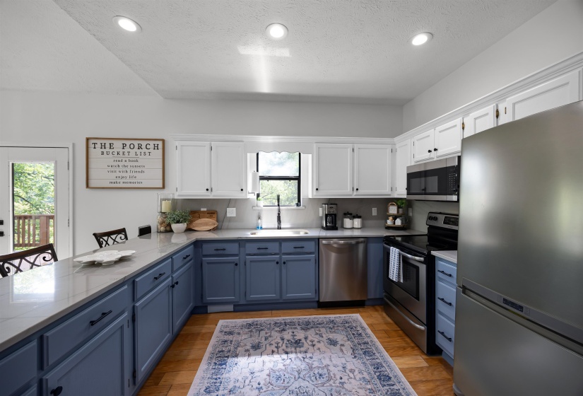 Kitchen featuring white upper and blue lower  cabinetry, quartzite countertops, stainless steel appliances, light wood-style floors, and a textured ceiling