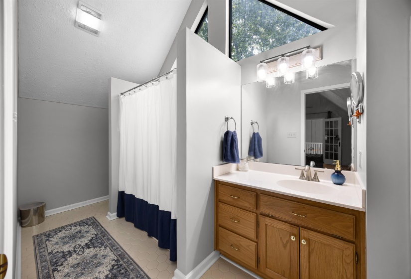 Full bathroom with vanity, light tile patterned flooring, vaulted ceiling