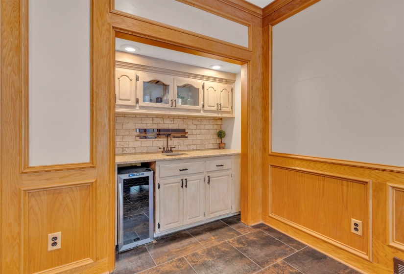 Built-in wet bar featuring a beverage cooler, light-toned cabinetry with glass-front accents, and a complementary stone tile backsplash