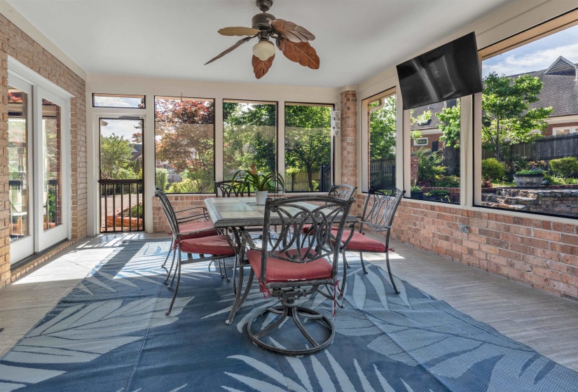 Brick-accented sunroom featuring large pane windows, a built-in ceiling fan, and access to the exterior