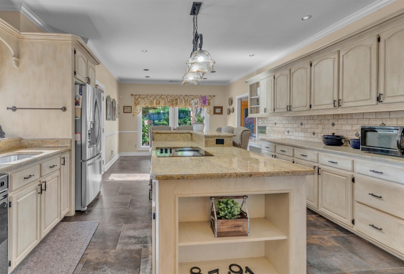 Kitchen featuring an island with an integrated cooktop, pendant lighting, light-toned cabinetry, granite countertops, and stone tile flooring