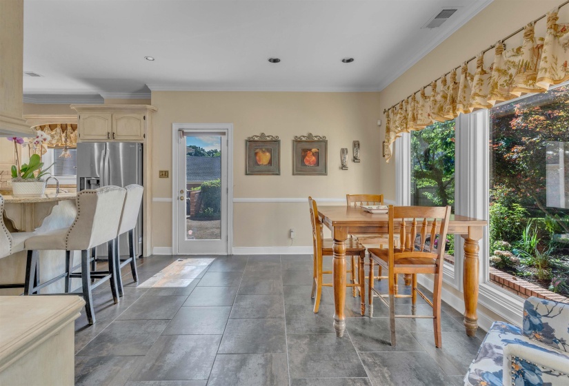 Kitchen and dining area featuring tile flooring, light-toned cabinetry, stainless steel refrigerator, and a window overlooking exterior landscaping