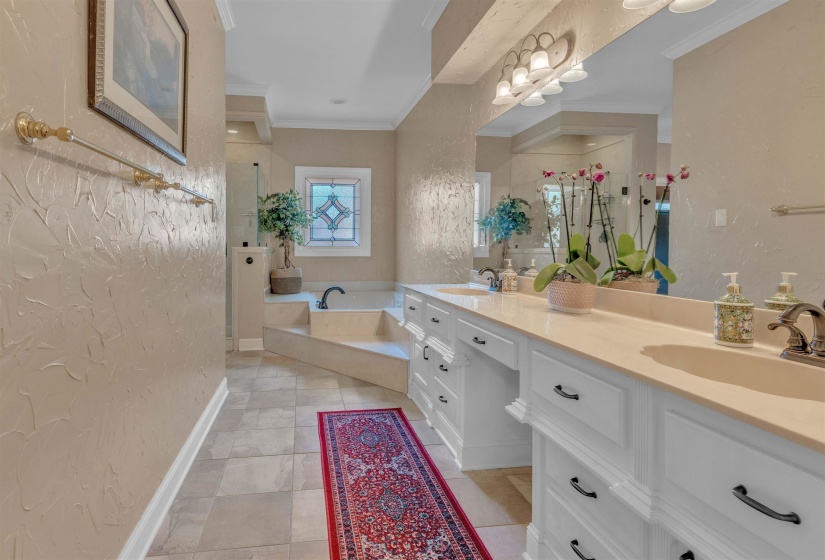 Spacious bathroom featuring a dual vanity with white cabinetry and light countertops, a built-in soaking tub with tiered steps, a separate glass-enclosed shower, and a decorative stained glass window