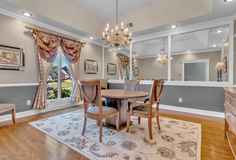 Formal dining area featuring rich wood-finish flooring, a tray ceiling, and a large window with white trim