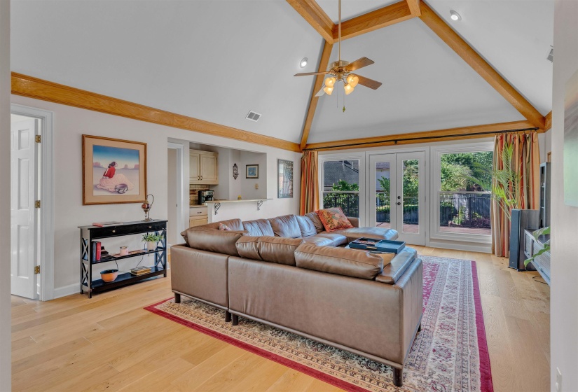 Vaulted ceiling featuring exposed wood beams, light wood-finish flooring, and French doors opening to an outdoor area