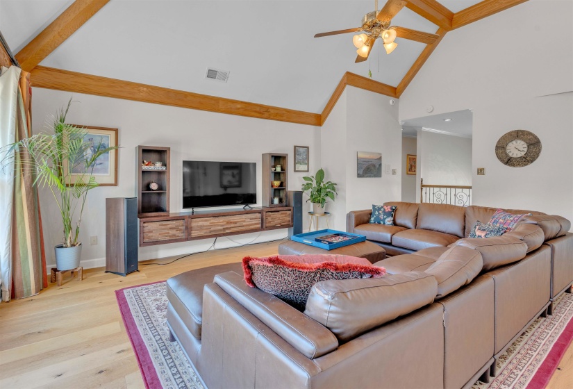 Living space featuring vaulted ceilings with exposed wood beams, a ceiling fan with light fixture, wood-finish flooring, and a built-in media console