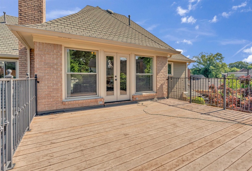 Expansive wood-finish deck featuring wrought iron railings and direct access to interior spaces through double glass doors