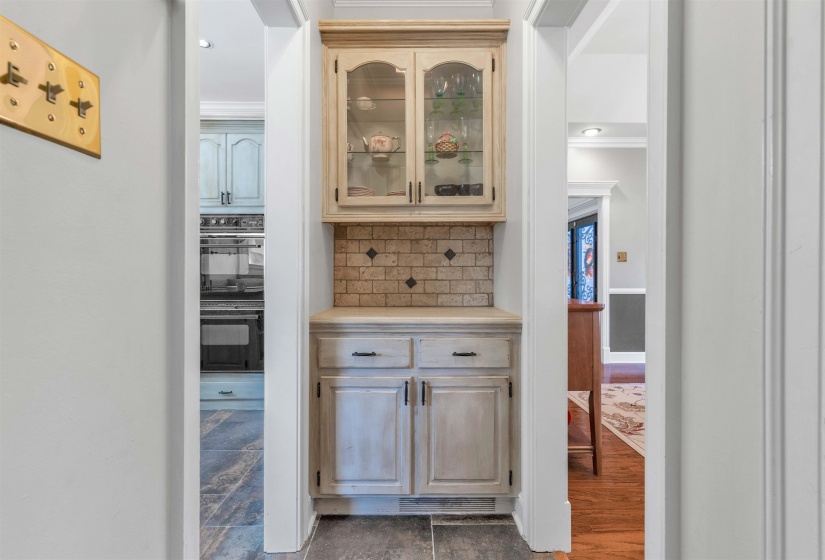 Built-in display cabinetry featuring glass-front uppers, a tiled backsplash with diamond accents, and lower storage cabinets with dark hardware