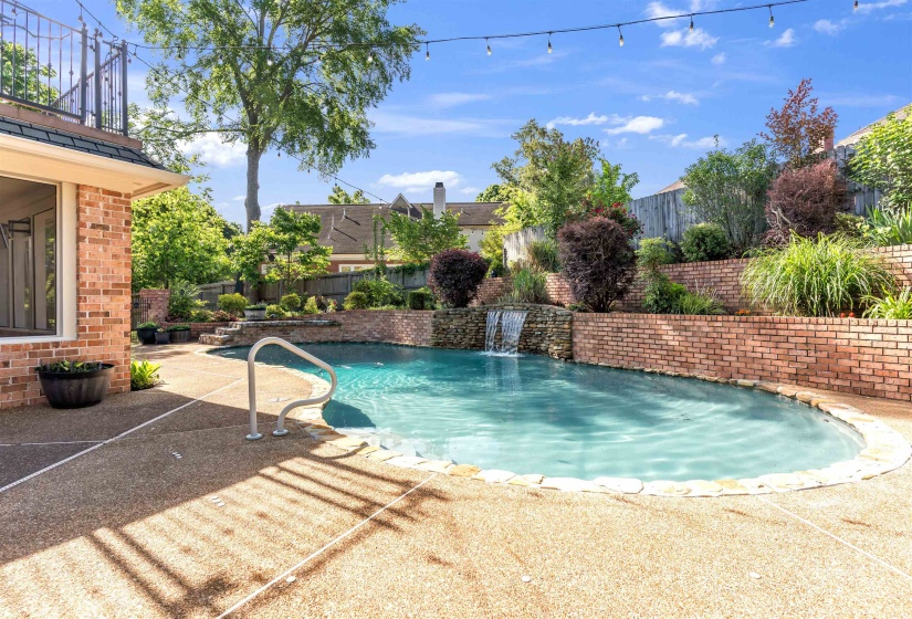 Outdoor swimming pool featuring a waterfall, integrated brick planters, and an exposed aggregate concrete deck