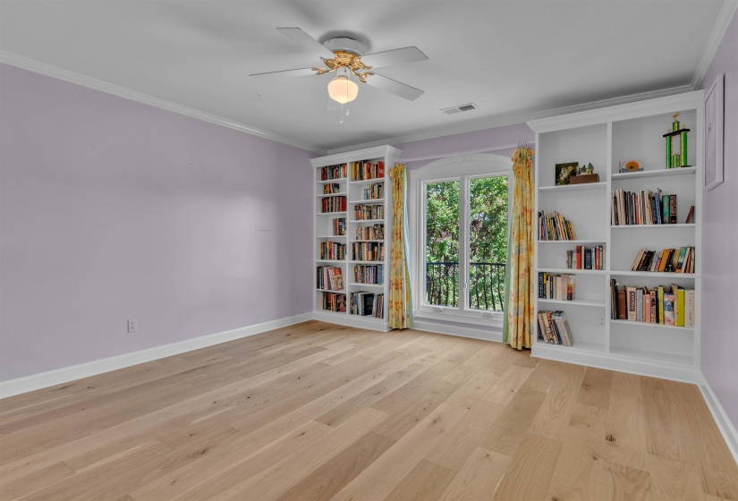 Room featuring hardwood flooring, built-in shelving, an arched window, crown molding, and a ceiling fan