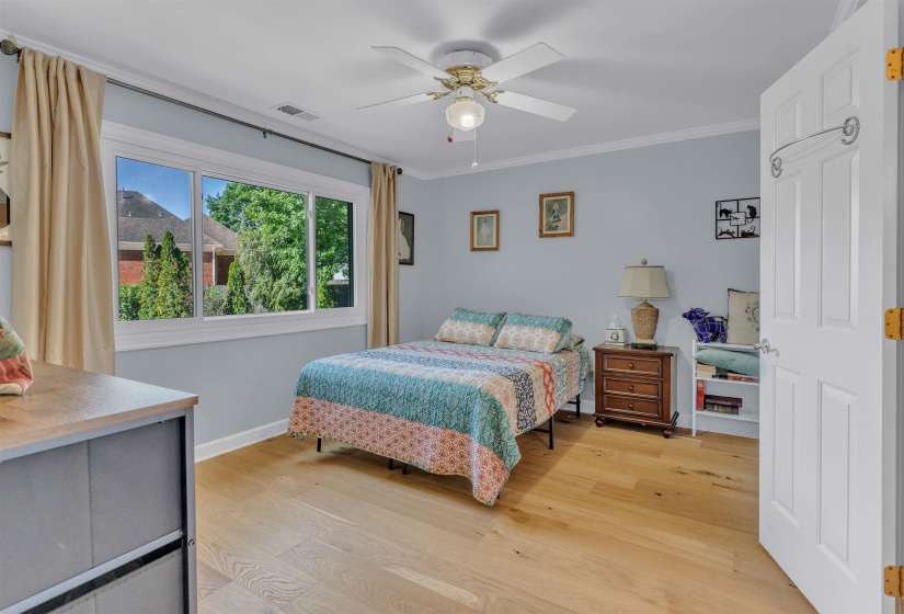 Bedroom featuring light wood-finish flooring, a multi-pane window, ceiling fan with integrated lighting, a built-in bookshelf, and light blue walls with white trim