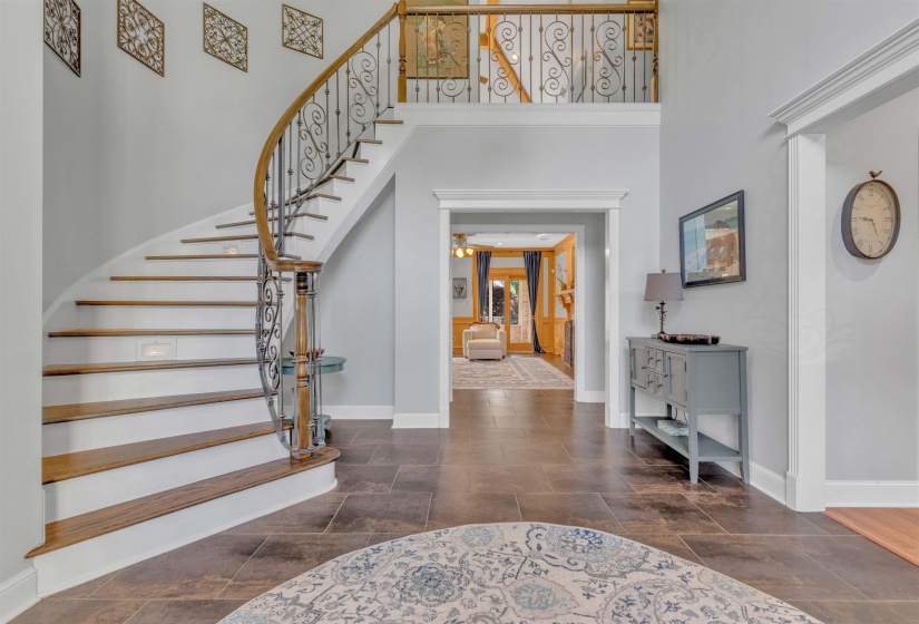 Grand foyer featuring a curved staircase with wood-finish treads, wrought iron balusters, and a matching wood-finish handrail