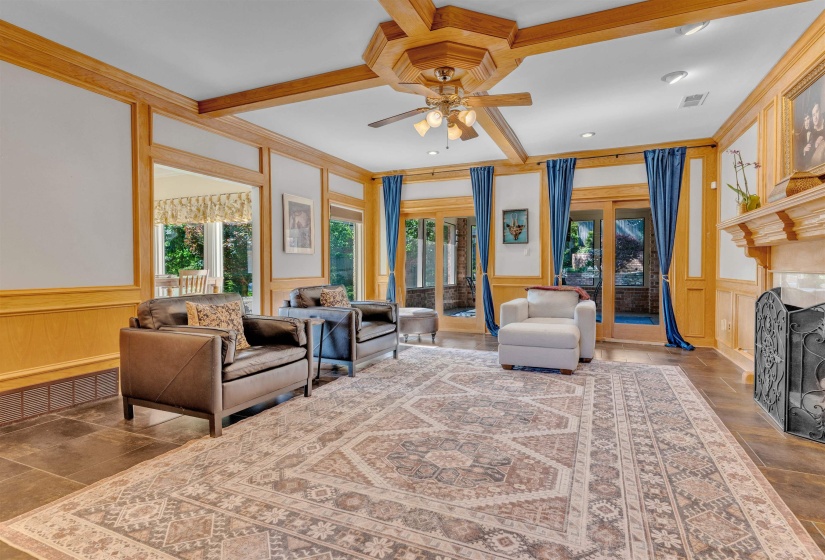 Expansive room featuring rich wood trim, exposed ceiling beams, a central ceiling fan with lighting, and multiple sets of glass panel doors
