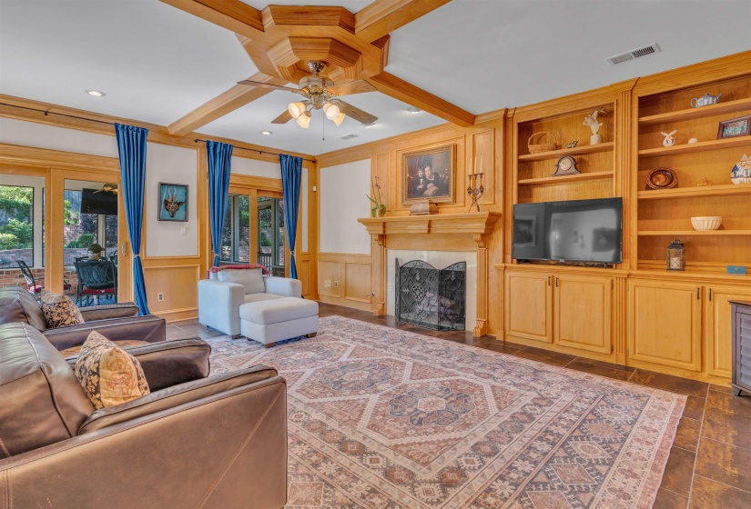 Spacious living area featuring extensive wood paneling and trim, a coffered ceiling with a ceiling fan, and built-in shelving units