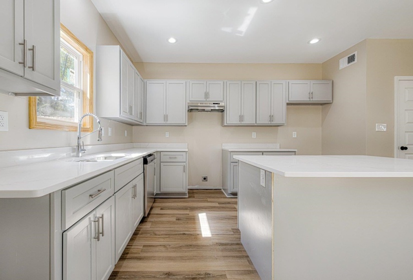 Kitchen with light wood-style flooring, light stone counters, recessed lighting, stainless steel dishwasher, and under cabinet range hood