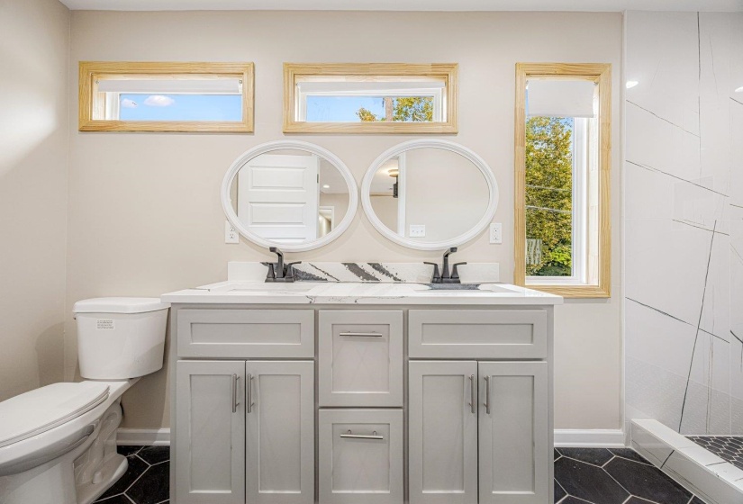 Full bath with double vanity, a shower stall, and dark tile patterned floors