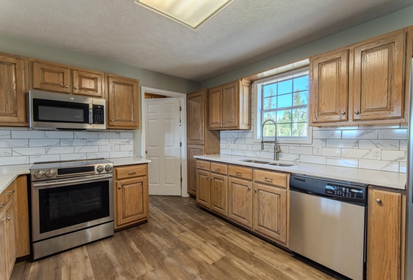 Kitchen featuring stainless steel appliances, backsplash, dark wood-style floors, a textured ceiling, and brown cabinets