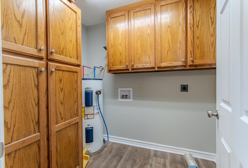 Washroom with light wood finished floors, cabinet space, electric water heater, electric dryer hookup, and hookup for a washing machine