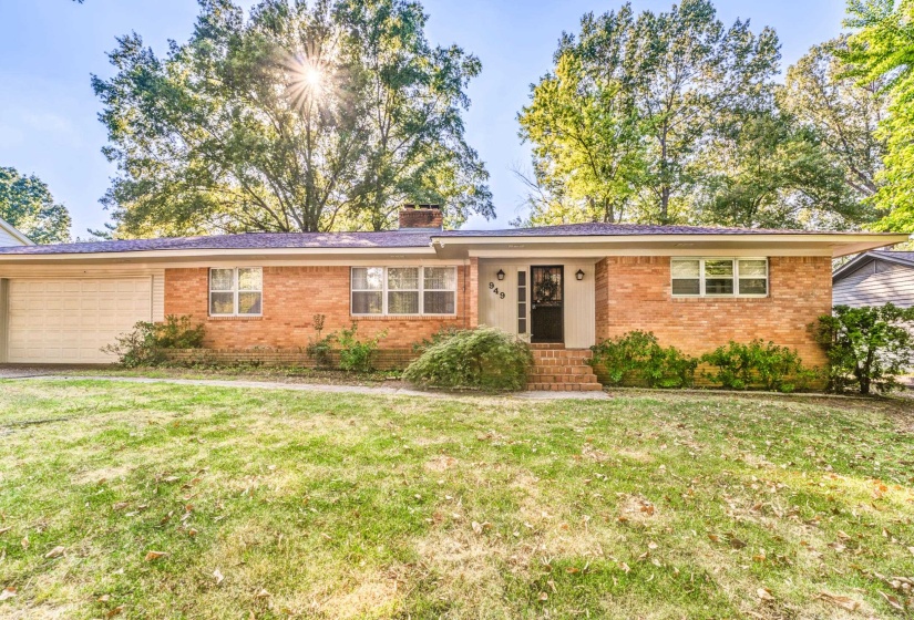 Ranch-style home featuring brick siding, a front yard, a chimney, and a garage