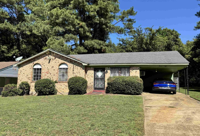 Single story home with a front lawn, brick siding, concrete driveway, and an attached carport