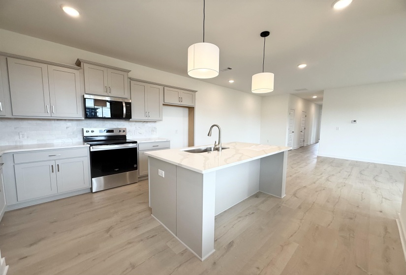 Kitchen featuring appliances with stainless steel finishes, backsplash, light wood finished floors, gray cabinetry, and light stone counters