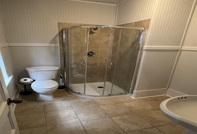 Bathroom with a stall shower, wood walls, and light tile patterned floors