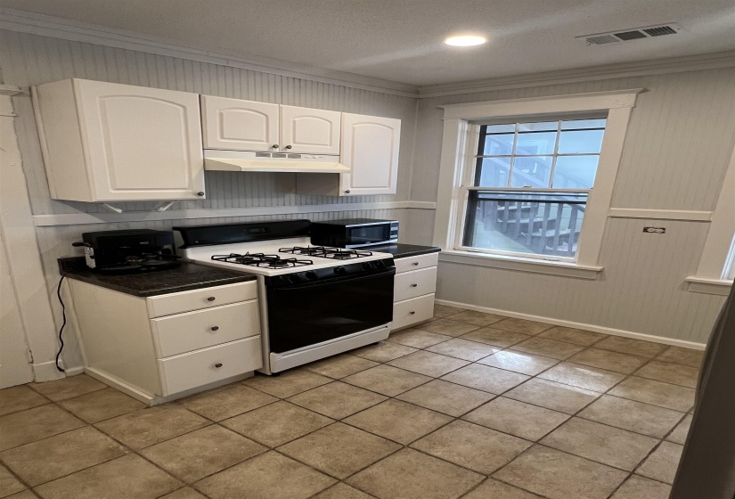 Kitchen featuring crown molding, gas stove, dark countertops, white cabinets, and wooden walls