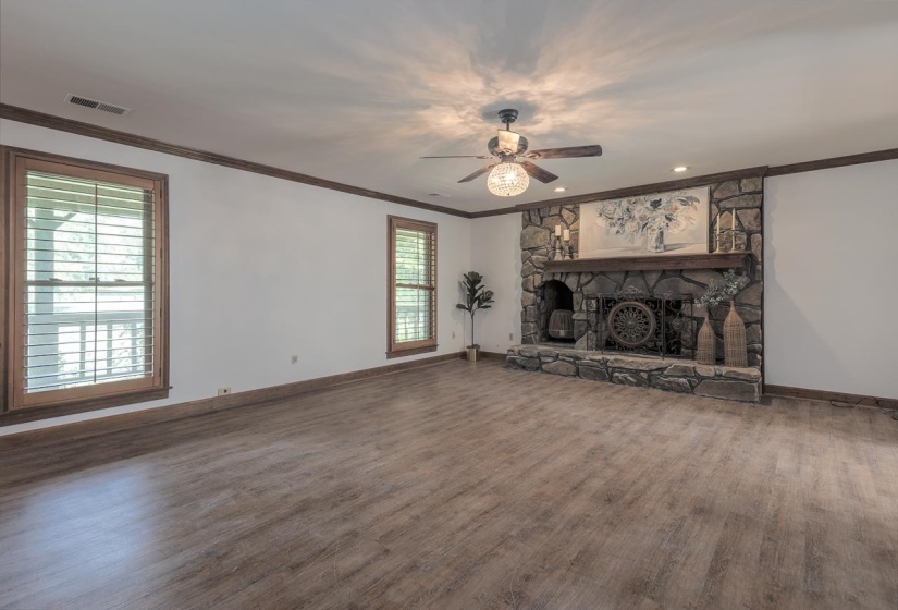 Unfurnished living room featuring crown molding, wood finished floors, a ceiling fan, a stone fireplace, and recessed lighting