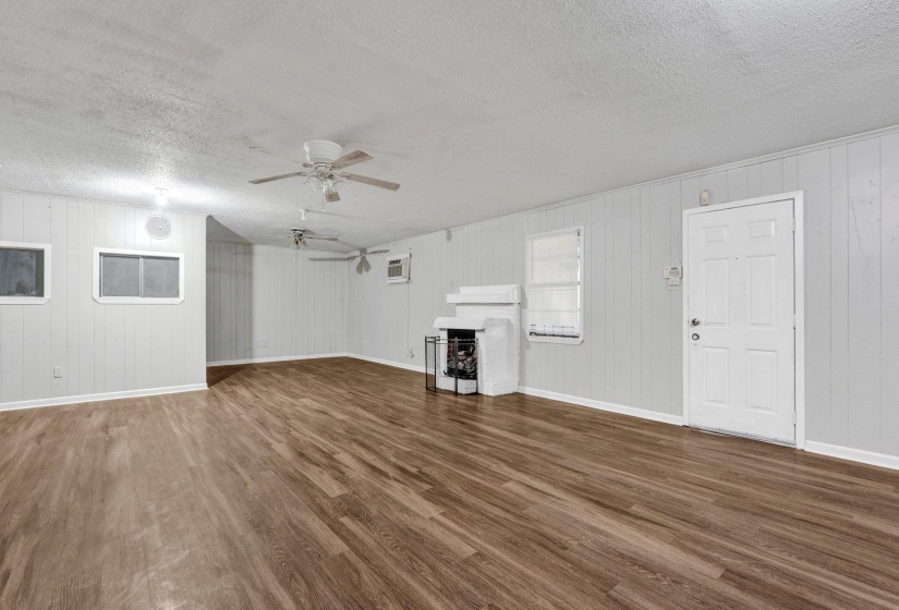 Unfurnished living room featuring ceiling fan, baseboards, a textured ceiling, and wood finished floors