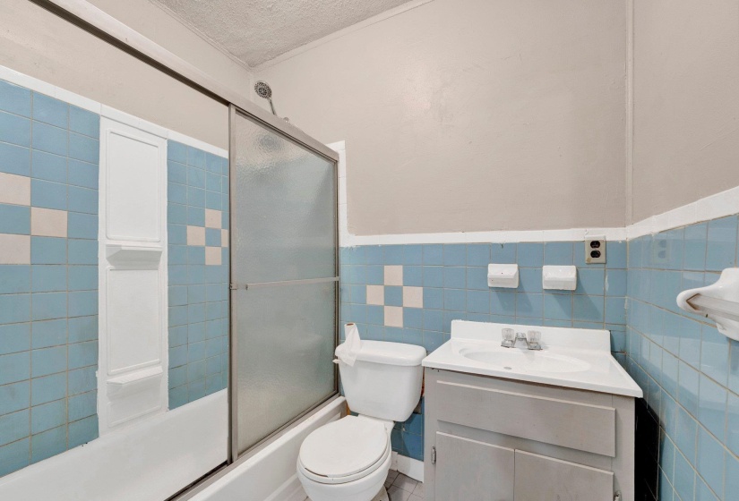 Bathroom with toilet, vanity, shower / bath combination with glass door, a textured ceiling, and tile walls