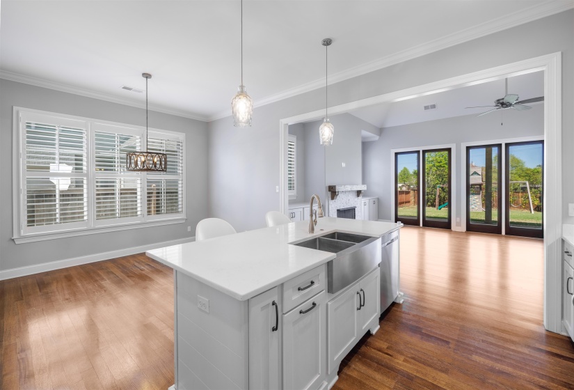 Kitchen with a kitchen island with sink, hanging light fixtures, white cabinetry, light stone countertops, and ornamental molding