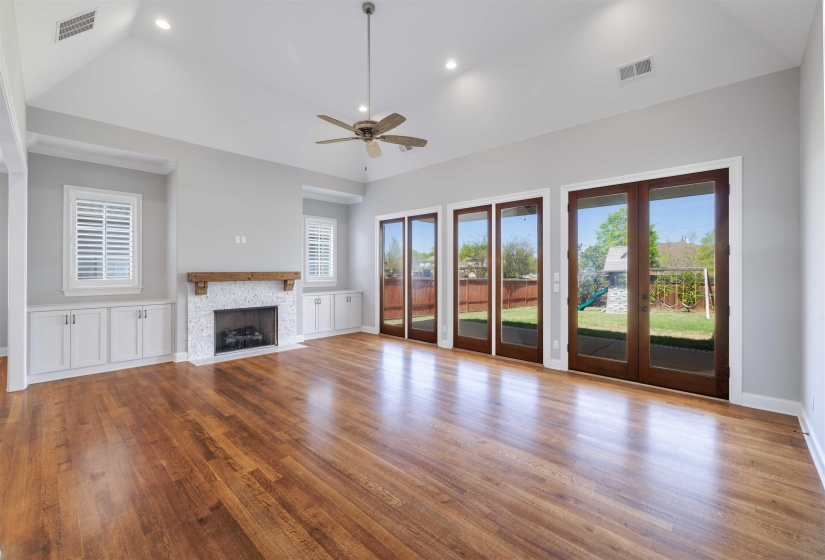 Unfurnished living room with a ceiling fan, french doors, light wood-type flooring, vaulted ceiling, and a fireplace
